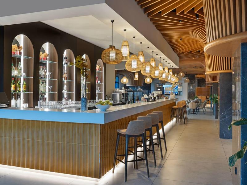 Moderní hotelový bar s dřevěným stropem, barovými židlemi a elegantním osvětlením.