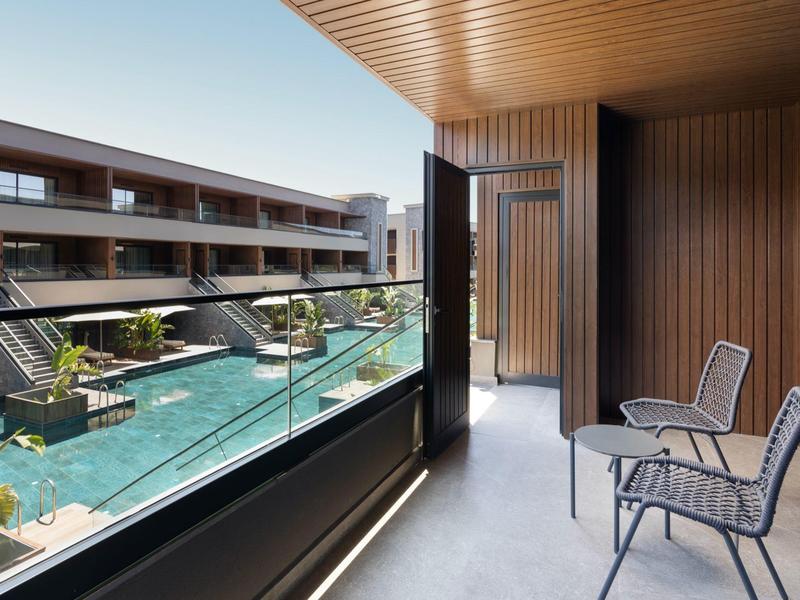 Balkon se židlemi a výhledem na hotelový bazén obklopený moderní dřevěnou budovou.