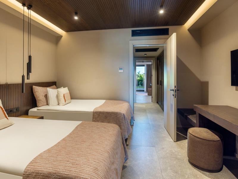 Moderní hotelový pokoj se dvěma postelemi, dřevěným nábytkem a TV s plochou obrazovkou.