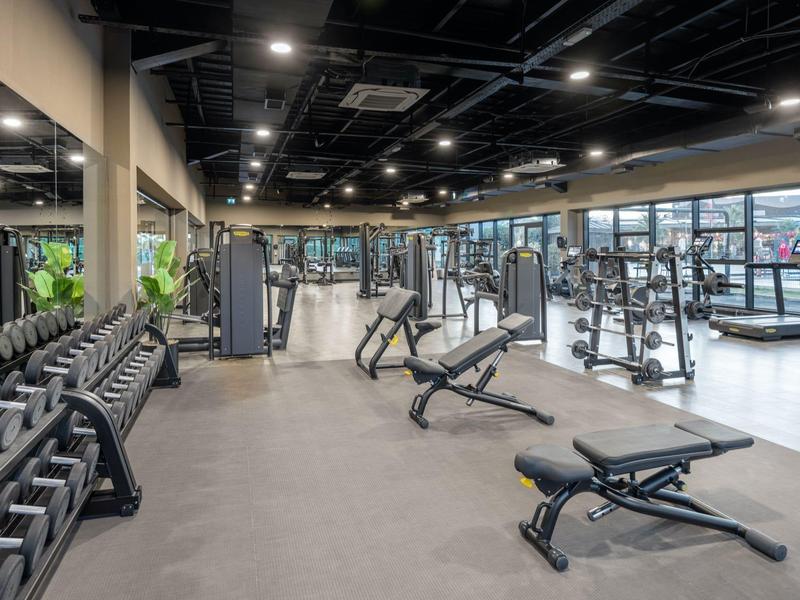 Moderní posilovna s činkami, tréninkovými stroji a lavičkami v světlém prostoru.