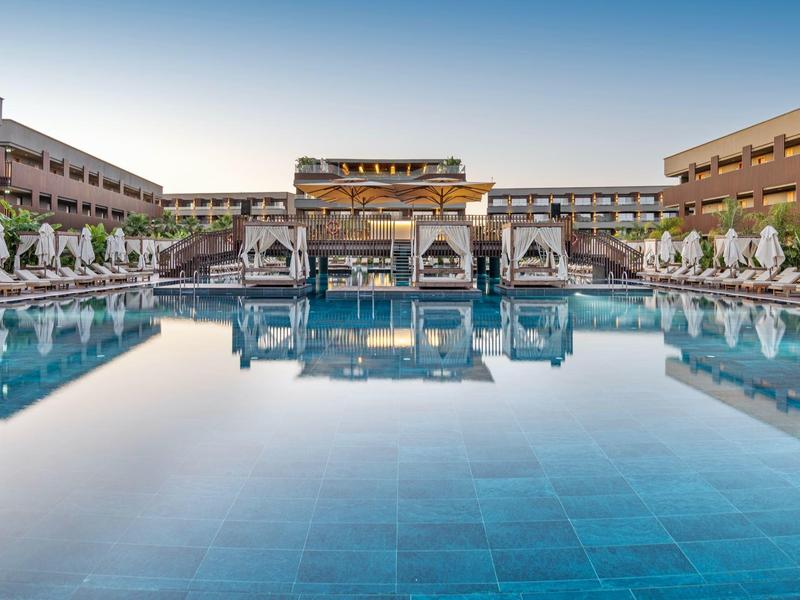Velký hotelový bazén s lehátky a slunečníky za jasné oblohy.