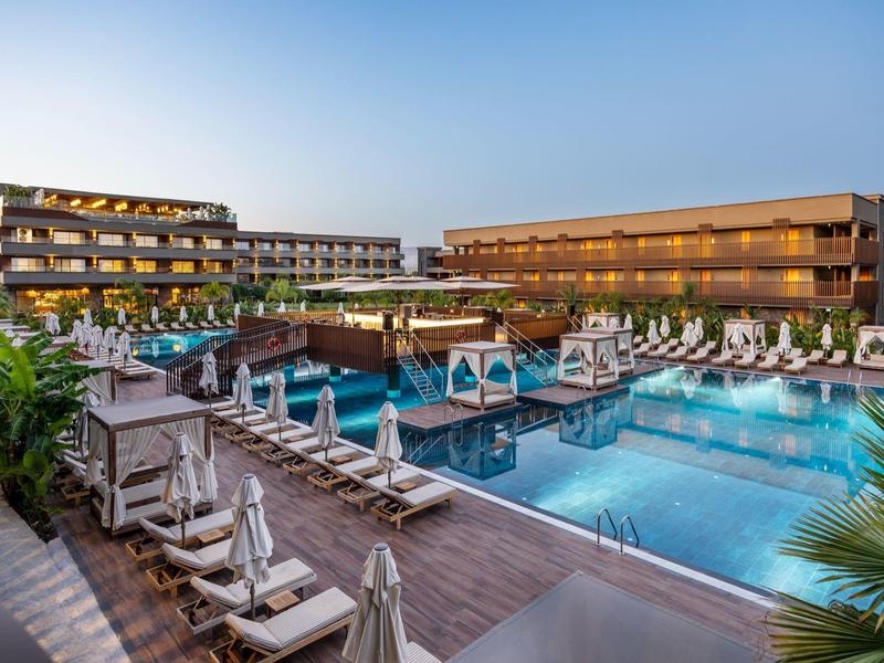 Moderní hotelový bazén s lehátky a slunečníky za jasného večera.