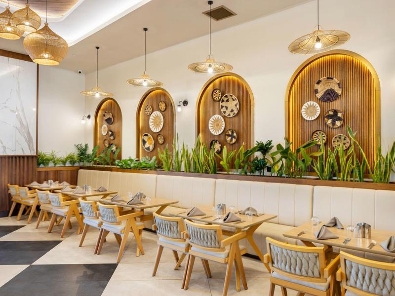 Moderní restaurace s dřevěnými židlemi, rostlinami a dekorativními oblouky na stěnách.