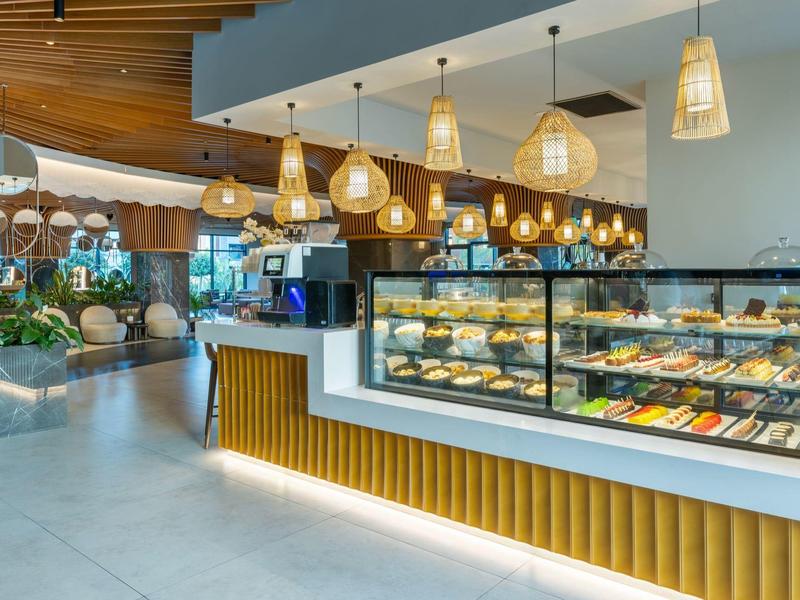 Moderní kavárna s osvětleným pultem a vitrínou plnou pečiva v světlém interiéru.