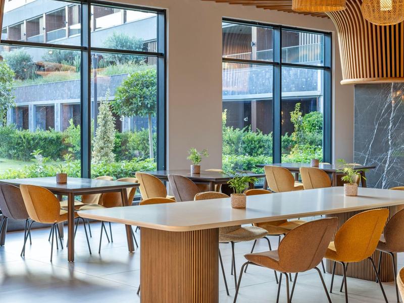 Moderní jídelna s velkým stolem, židlemi a výhledem na zahradu a budovu.