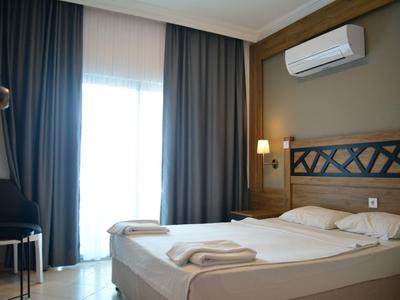 Camera d'albergo moderna con letto matrimoniale, condizionatore e tende scure davanti a finestra luminosa.