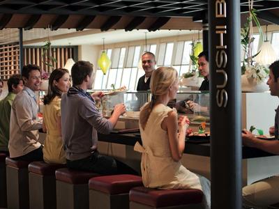 Menschen sitzen an einer Sushi-Bar und essen gemeinsam in einem modernen, gut beleuchteten Restaurant.