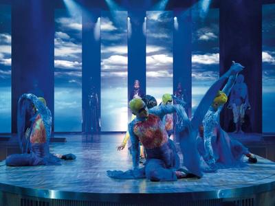 Drei Künstler in blauer Beleuchtung führen eine Tanzperformance auf einer runden Bühne auf.