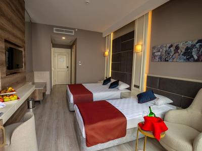 Modern eingerichtetes Hotelzimmer mit zwei Betten, roten Bettdecken und gemütlichem Sessel.