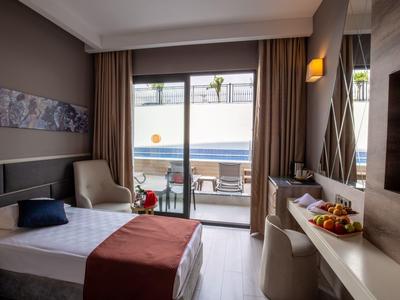Modernes Hotelzimmer mit Einzelbett, Schreibtisch, Sessel und Terrasse mit Blick auf den Pool.