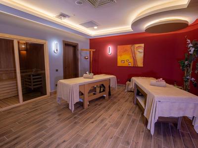 Innenraum eines Massageraums mit zwei Behandlungsliegen, Holzboden und roter Wanddekoration.