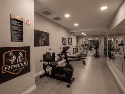 Moderner, schmaler Fitnessraum mit stationärem Fahrrad, Gewichten und großen Spiegeln an der Wand.