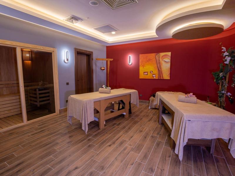 Une pièce bien-être calme avec deux tables de massage et un sauna en arrière-plan.