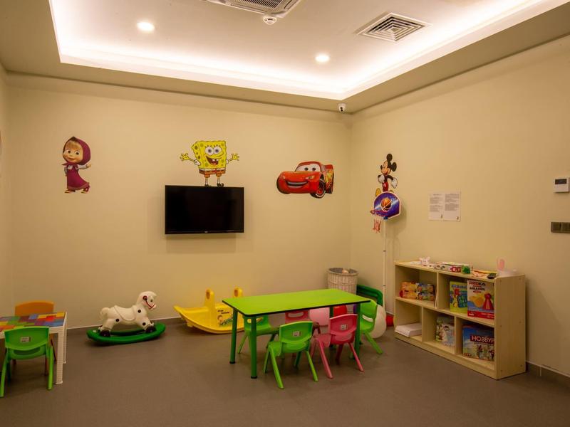 Salle de jeux pour enfants avec mobilier coloré, décorations murales et étagère à jouets.
