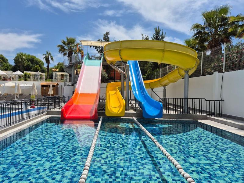 Des toboggans colorés mènent à une piscine claire avec des palmiers et un ciel bleu en arrière-plan.