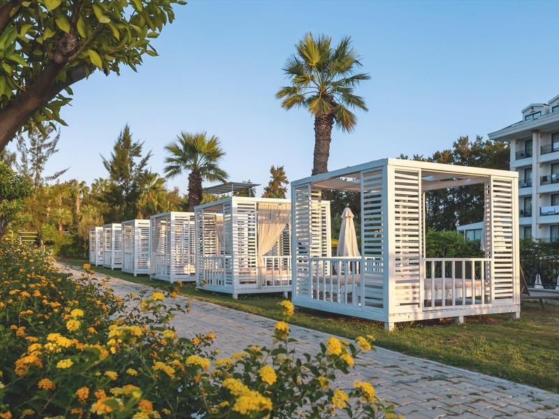 Des pavillons blancs de détente alignés à côté d'un jardin fleuri et d'un hôtel.