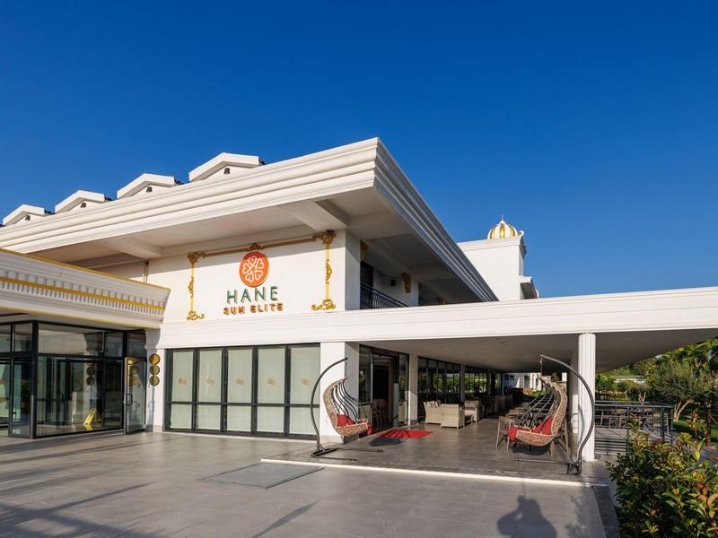 Bâtiment d'hôtel moderne avec terrasse ouverte et chaises suspendues sous un ciel bleu.