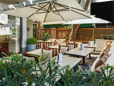 Gemütliche Terrasse mit Polstersesseln, Tischen aus Stein und großem Sonnenschirm, umgeben von Pflanzen.