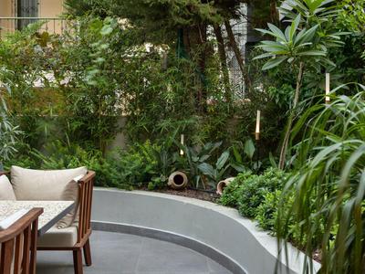 Gemütliche Gartenecke mit weißem Rundsofa, Holztisch und üppigem, grünem Pflanzenwuchs.