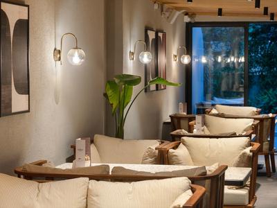 Gemütlicher Raum mit hellen Sofas, Wandlampen, Pflanzen und großem Fenster mit Abendblick.