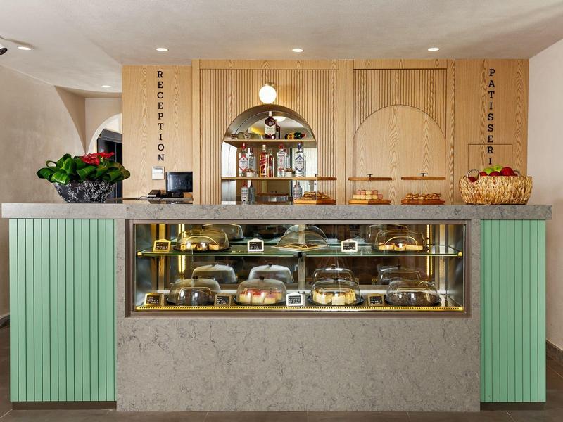 Kuchenladen mit gläserner Theke, grünen Seitenverkleidungen und Holzdekor an der Wand.