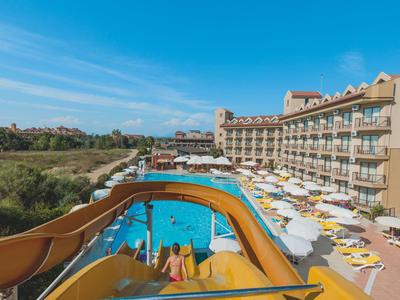 Large hotel pool with water slide and sun loungers under sunny weather.