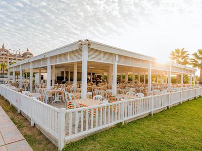 Large covered terrace with tables and chairs next to a hotel and lawn