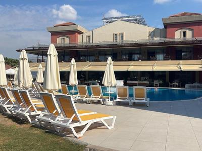 Rows of lounge chairs and umbrellas next to a pool in front of a hotel building under blue sky.