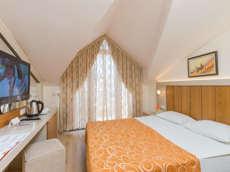 Cozy hotel room with double bed, TV, kettle, and a view of a triangular window.