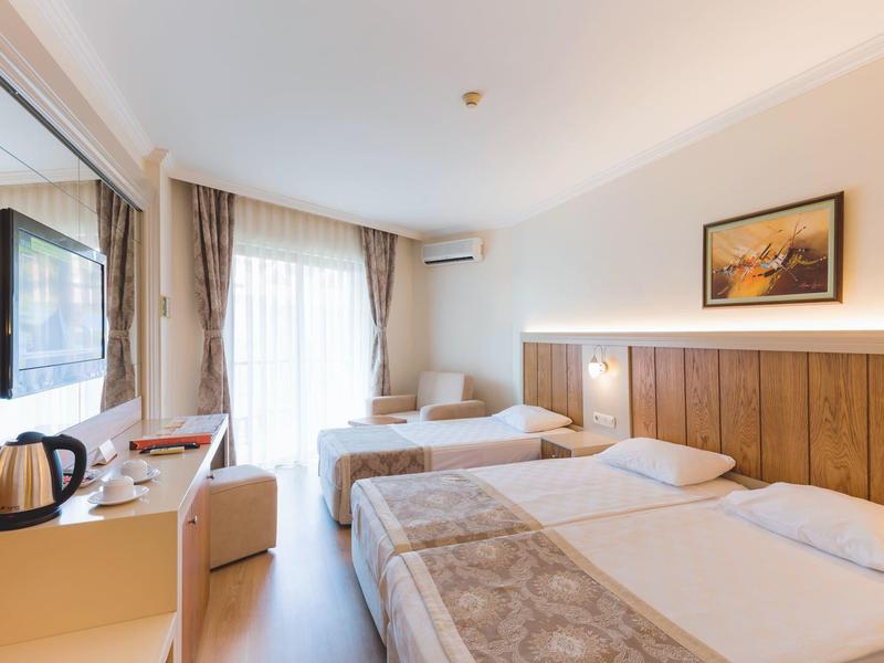 Bright hotel room with two beds, nightstand, TV, desk, and window with curtains.