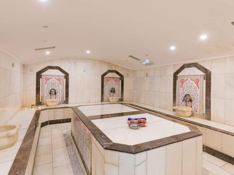 Bright, luxurious hammam with marble basin and intricate wall decorations.