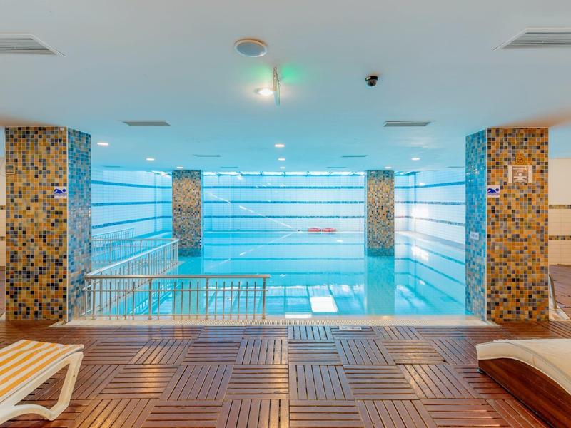 Modern indoor pool with wooden floor and lounge chairs in a hotel.