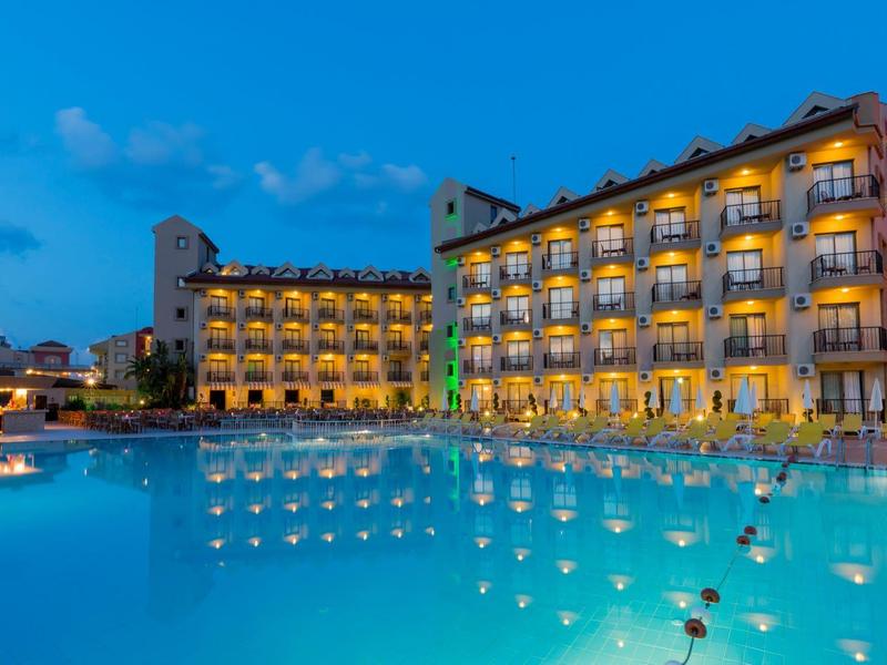 Modern hotel with illuminated balconies and large outdoor pool at dusk.