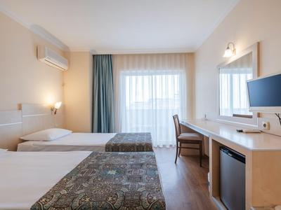 Chambre d'hôtel lumineuse avec deux lits simples, bureau, chaise, télévision et climatisation.