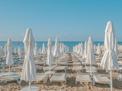Plage avec des chaises longues blanches et des parasols fermés sous un ciel bleu.