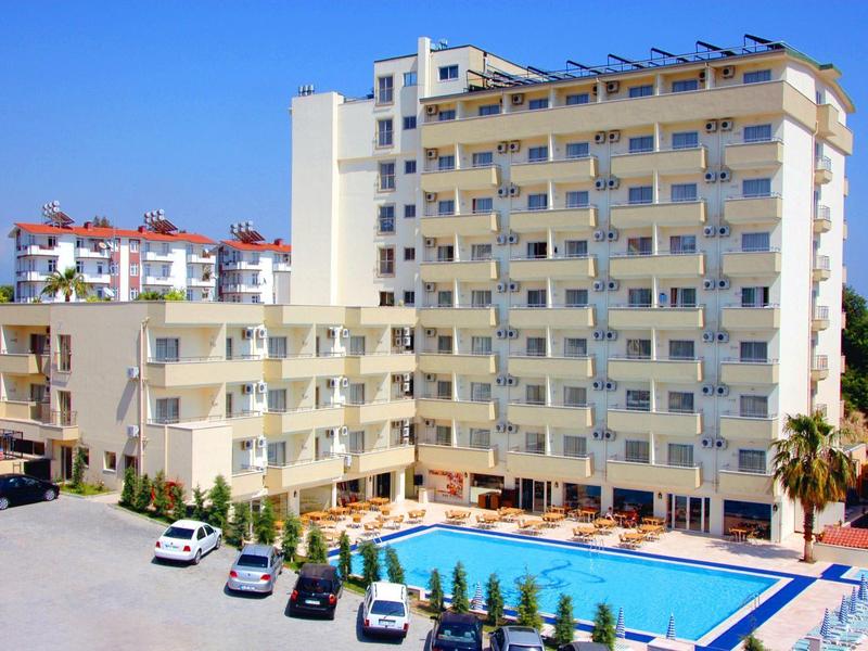 Alto edificio dell'hotel con piscina all'aperto, lettini e auto parcheggiate sotto un cielo sereno.