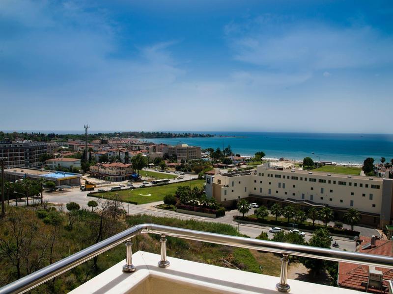 Vista dal balcone su edifici cittadini, strade e mare sotto un cielo sereno.