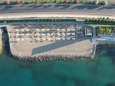 Aerial view of a sandy beach with sun loungers beside calm sea and road in the background.