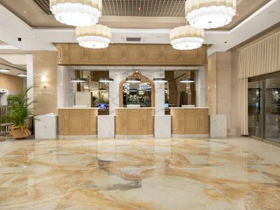 Bright hotel lobby with marble floor, wooden reception desk, and large chandeliers.