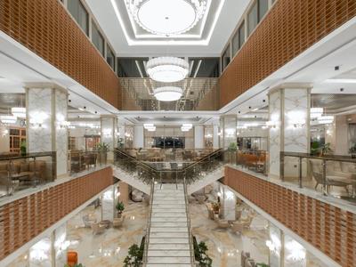 An elegant hotel interior featuring a central staircase, marble floors, and modern lighting.