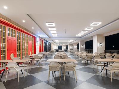 Modern hotel terrace with numerous tables and chairs, bright ambiance, and a red accent wall.