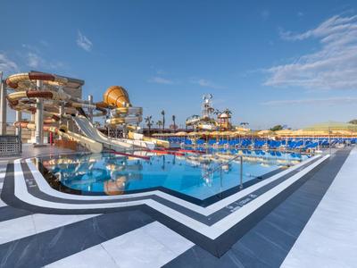 Large outdoor pool with water slides and sun umbrellas at a hotel resort under clear sky.