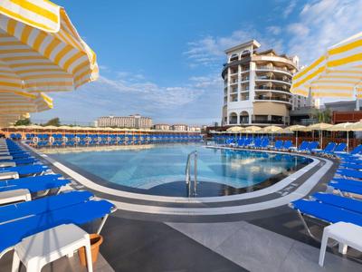 Large outdoor pool with blue loungers and yellow-white umbrellas under clear sky.