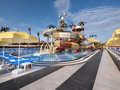 A large water park with water slides, pools, and yellow umbrellas shading lounge chairs under blue sky.