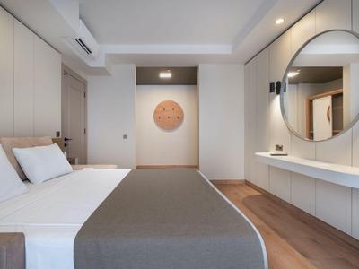 Modern hotel room with double bed, gray bedspread, large round mirror, and wooden floor.