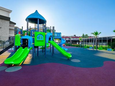 Bunter Kinderspielplatz mit Rutschen und Klettermöglichkeiten neben einem Hotelgebäude bei sonnigem Wetter.