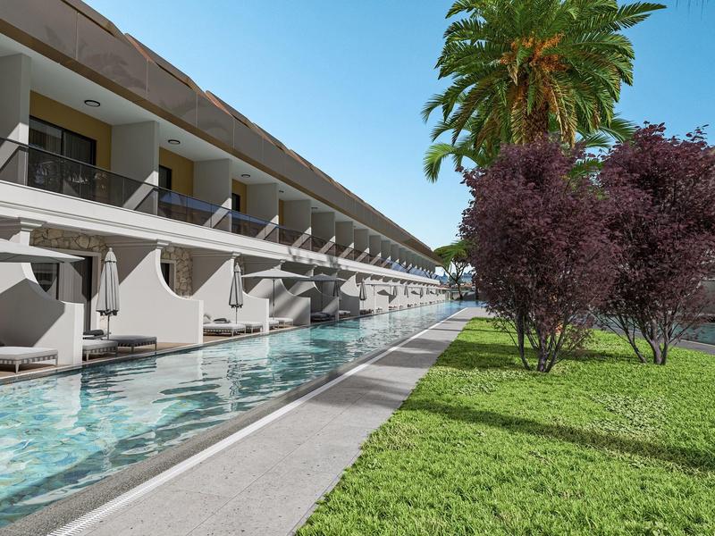 Hotel moderno con camere che si affacciano su una lunga piscina stretta e un prato verde con alberi