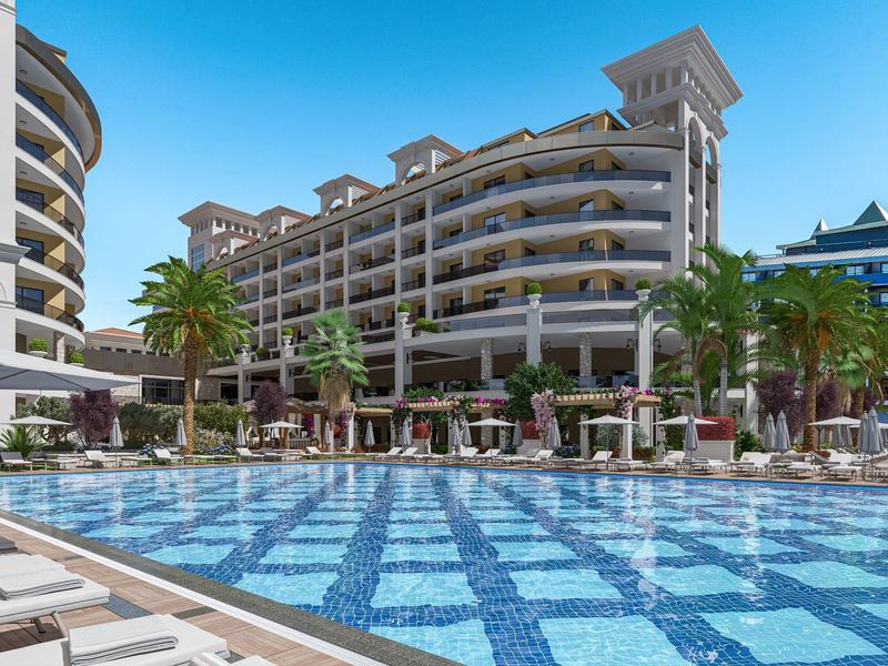 Grande hotel con piscina all'aperto, palme e lettini sotto ombrelloni.