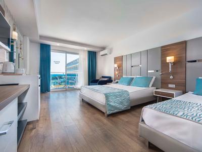 Chambre d'hôtel moderne avec lit double et simple, sol en bois et balcon avec vue sur la mer.