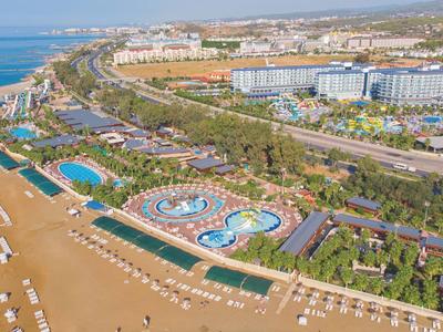 Vue aérienne d'un complexe de plage de villégiature avec piscines, bâtiments et zone de plage le long de la côte.